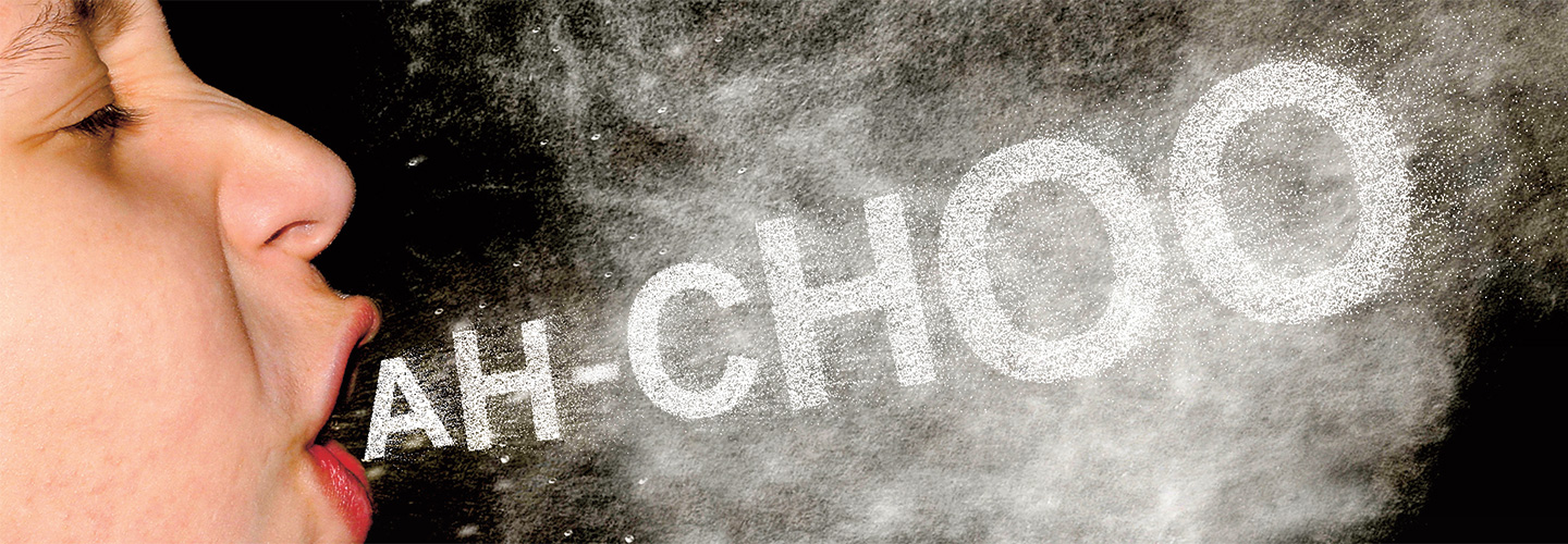 A child sneezing and a cloud of saliva particles comes out of his mouth with the word "Ah-choo".