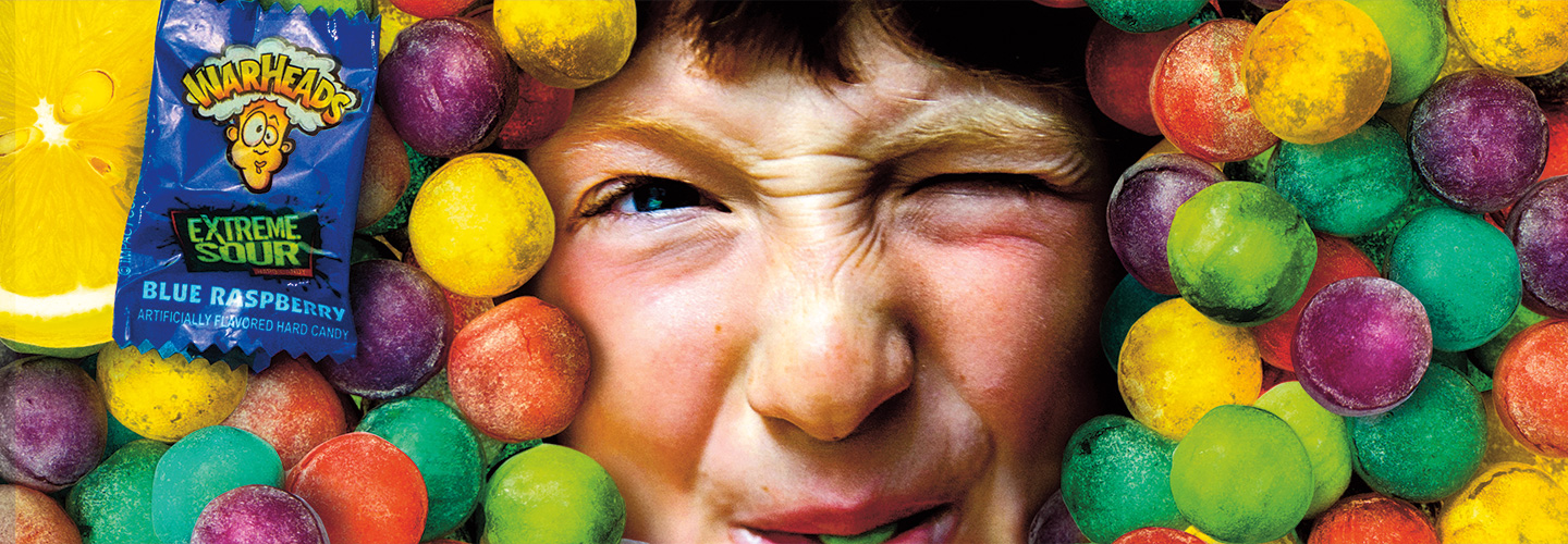 The face of a kid puckering his mouth, surrounded by multi-colored sour candy